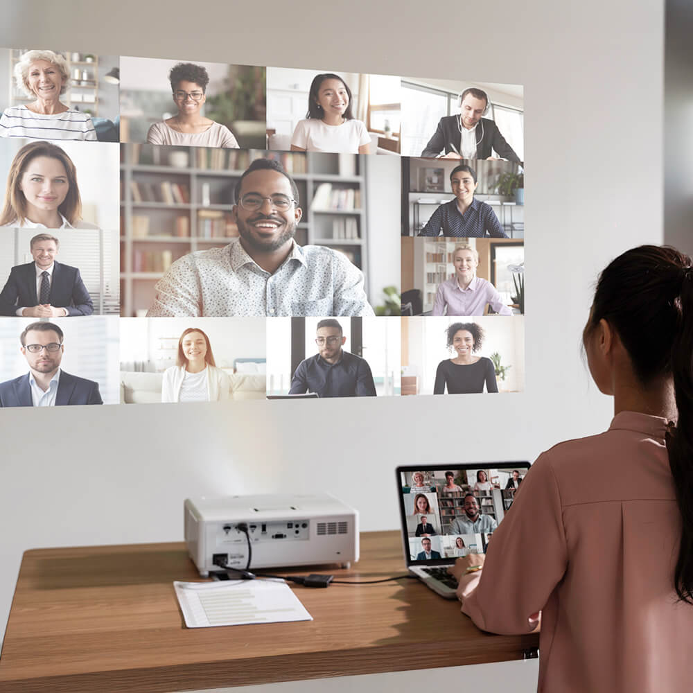 Woman attending a virtual meeting in a home office using a short throw projector displaying multiple people on a wall — perfect for remote work, video conferencing, and productivity.